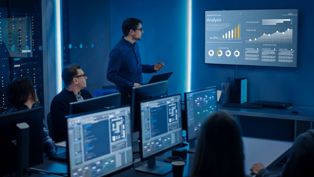 Team of Professional IT Developers Have a Meeting, Speaker Shows Growth Data with Graphs, Charts, Software UI. Shown on TV. Concept: Software UI Development, Deep Learning, Graphs, Charts.