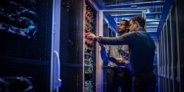 Two male IT engineers checking servers in server room with help of tablet.